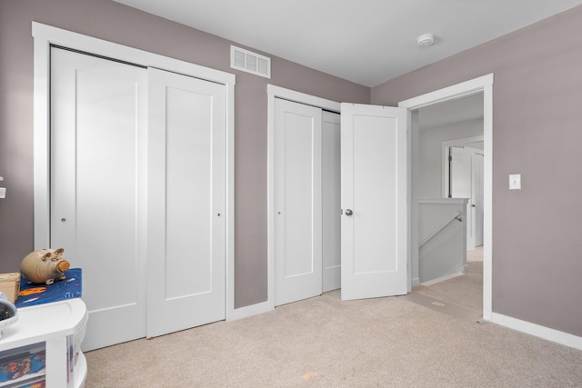 unfurnished bedroom with two closets, carpet, and baseboards
