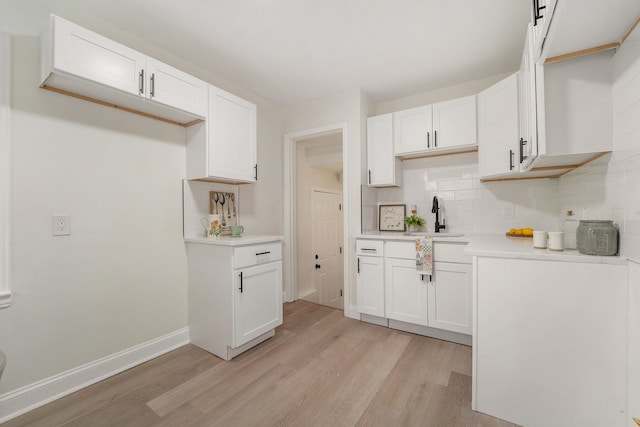 kitchen featuring light wood-style flooring, a sink, tasteful backsplash, and white cabinets