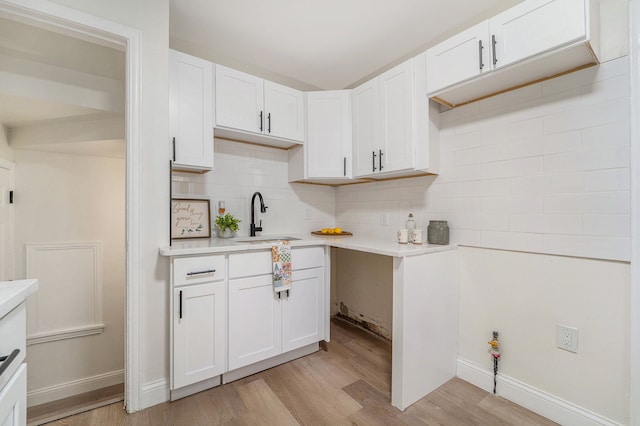kitchen with a sink, light countertops, light wood-style floors, decorative backsplash, and white cabinets