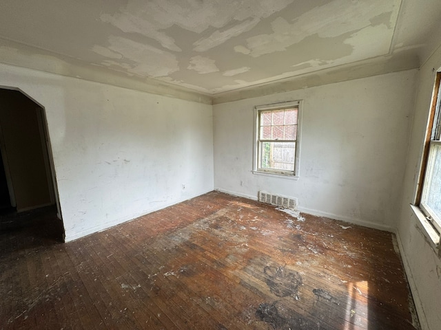 spare room featuring hardwood / wood-style flooring, arched walkways, and baseboards