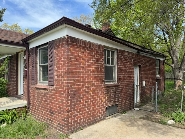 view of property exterior featuring brick siding, a gate, and a chimney