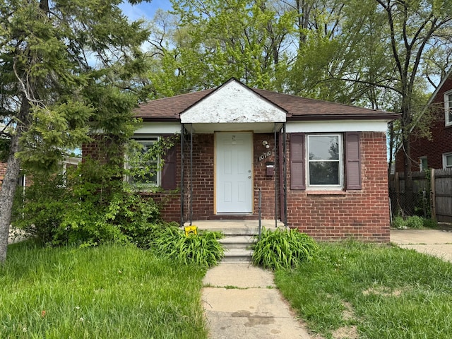 bungalow featuring fence, brick siding, and roof with shingles