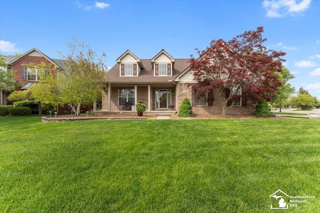 25345 Hunter Ln, Flat Rock, MI 48134 - new england style home featuring brick siding, a front yard, covered porch, and a shingled roof