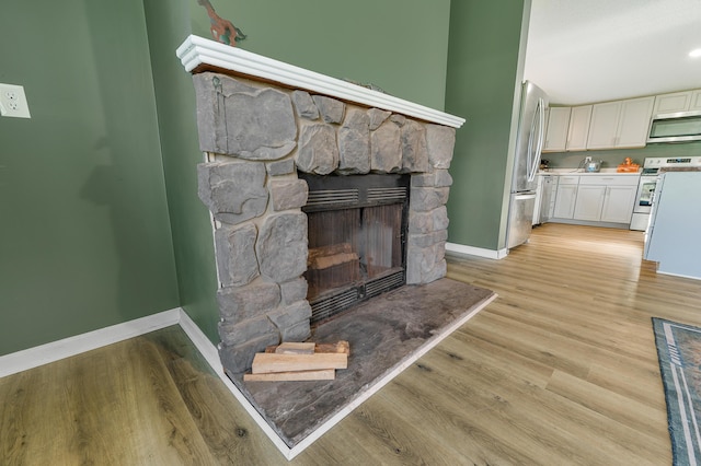 3311 5 Mile Rd, Sears, MI 49679 - detailed view of stainless steel appliances, baseboards, a fireplace, and wood finished floors