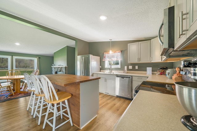 3311 5 Mile Rd, Sears, MI 49679 - kitchen with stainless steel appliances, wood counters, a breakfast bar area, light wood-style flooring, and decorative light fixtures