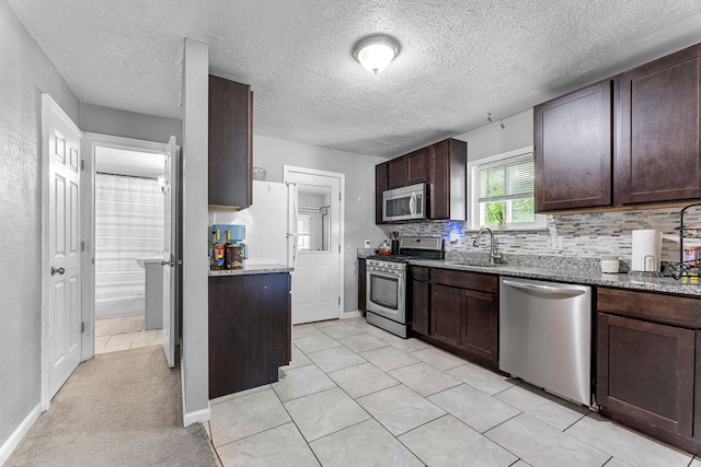 kitchen with stainless steel appliances, dark brown cabinets, tasteful backsplash, stone countertops, and a sink