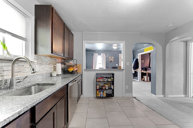 kitchen with a sink, stainless steel dishwasher, decorative backsplash, a textured ceiling, and dark brown cabinets