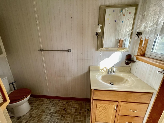 bathroom with vanity, toilet, wooden walls, and baseboards