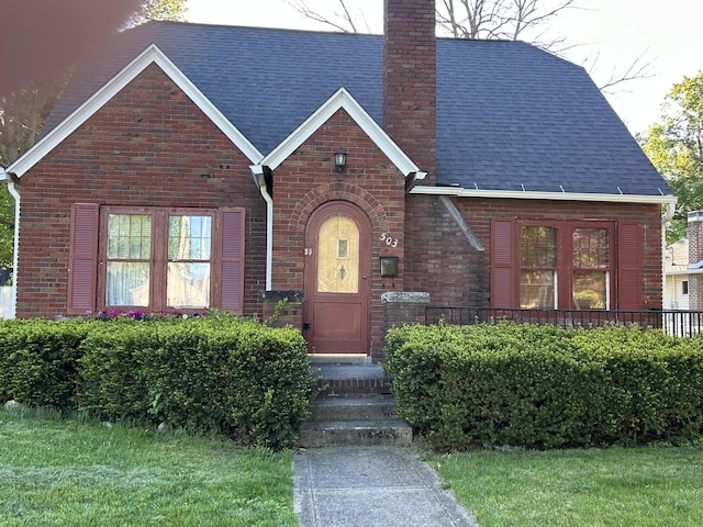 tudor-style house with brick siding, a chimney, and a shingled roof
