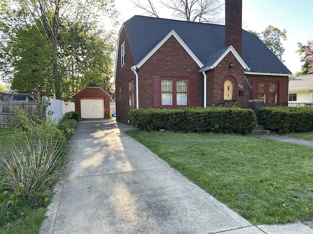 tudor home featuring brick siding, an outdoor structure, a detached garage, concrete driveway, and a chimney