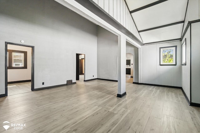 1418 Sunnyside Ave, Flint, MI 48503 - unfurnished living room featuring arched walkways, a towering ceiling, light wood-type flooring, and baseboards