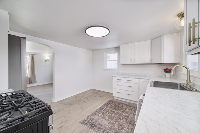 923 Maple St, Ludington, MI 49431 - kitchen featuring a sink, gas range, arched walkways, white cabinets, and light wood-style flooring
