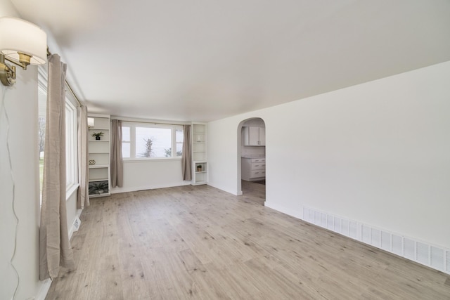 923 Maple St, Ludington, MI 49431 - unfurnished living room featuring arched walkways, light wood finished floors, and baseboards