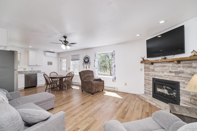 2073 Gunn Rd, Manistee, MI 49660 - living room featuring baseboard heating, a wall mounted AC, light wood-style floors, a stone fireplace, and a ceiling fan