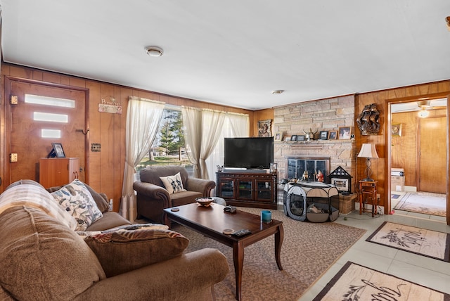 living room with wooden walls, a stone fireplace, and tile patterned floors