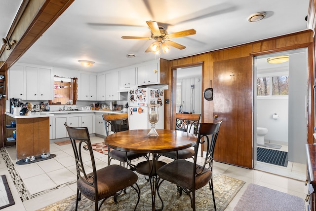 dining area with ceiling fan, light tile patterned flooring, and wood walls