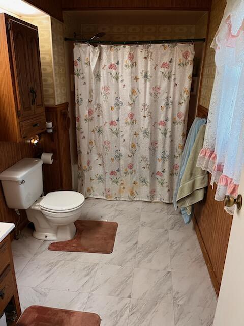 1116 Atlantic St NW, Grand Rapids, MI 49504 - bathroom featuring wood walls, vanity, toilet, marble look tile flooring, and a shower with curtain