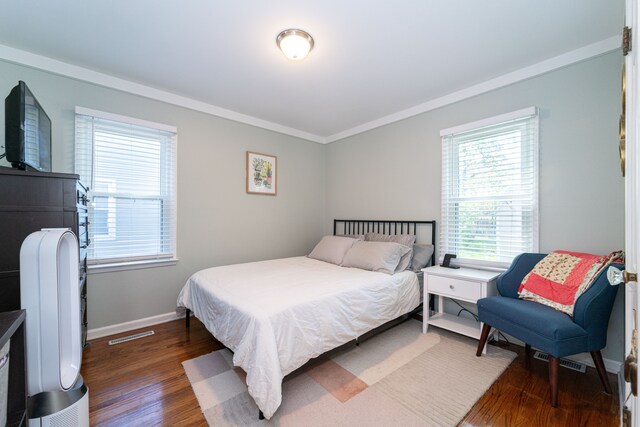 bedroom with wood finished floors, multiple windows, baseboards, and crown molding