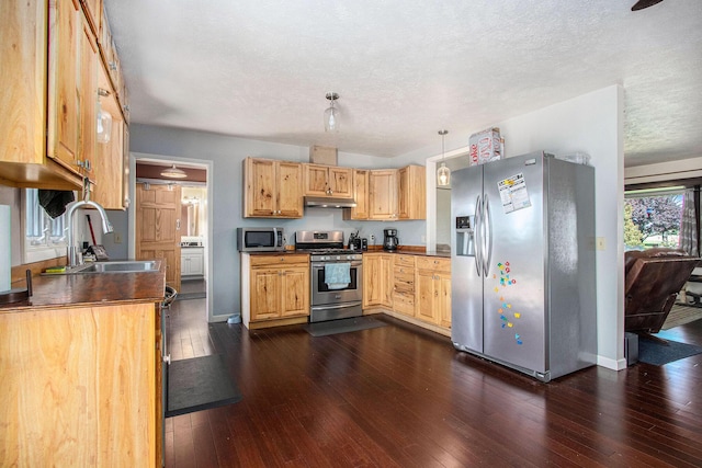 kitchen featuring appliances with stainless steel finishes, a sink, under cabinet range hood, dark wood-style floors, and dark countertops
