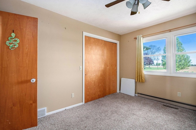 unfurnished bedroom with carpet flooring, a closet, baseboard heating, a ceiling fan, and a textured ceiling