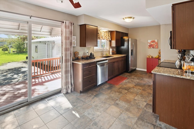 kitchen featuring stainless steel appliances, a sink, stone finish floors, baseboards, and light stone countertops