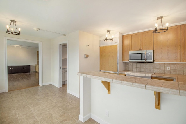 555 E William St Unit 25J, Ann Arbor, MI 48104 - kitchen with stainless steel microwave, a chandelier, range, backsplash, and baseboards