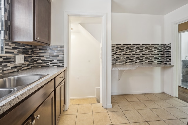 kitchen with light tile patterned floors, backsplash, dark brown cabinets, and a sink