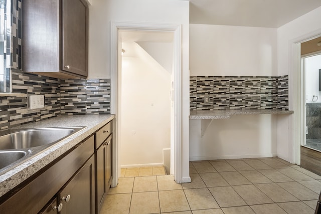 kitchen with light tile patterned flooring, backsplash, dark brown cabinets, light countertops, and a sink