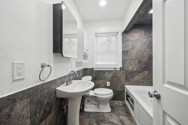 bathroom with tile walls, toilet, stone finish flooring, a tub, and wainscoting