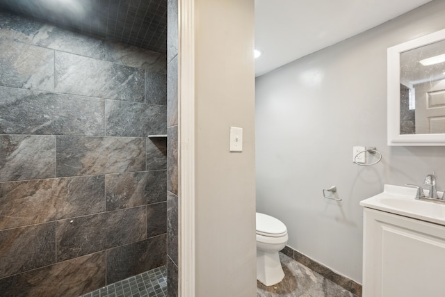 bathroom with toilet, a tile shower, vanity, and baseboards