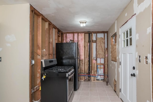 kitchen with stainless steel gas range oven, light tile patterned floors, and freestanding refrigerator