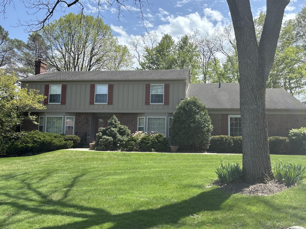 colonial house with brick siding, a chimney, and a front yard