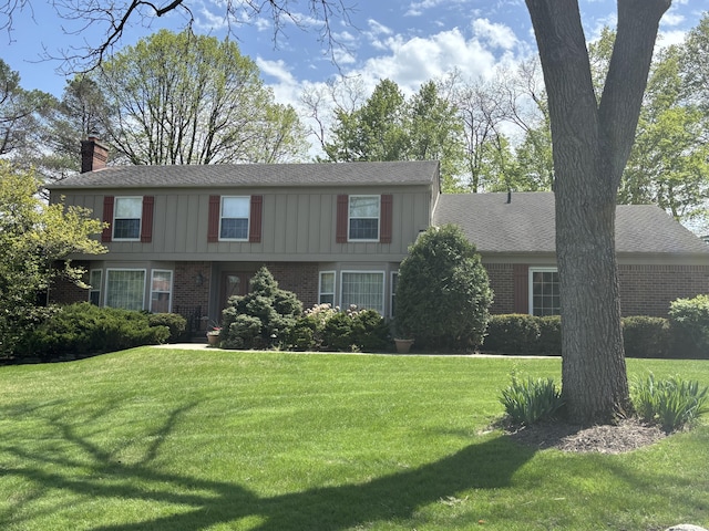 colonial house with brick siding, a chimney, and a front yard
