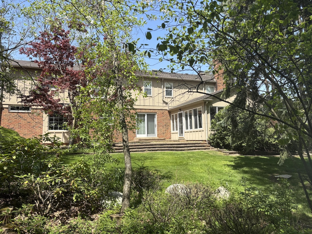 back of house featuring brick siding, a lawn, a chimney, and board and batten siding