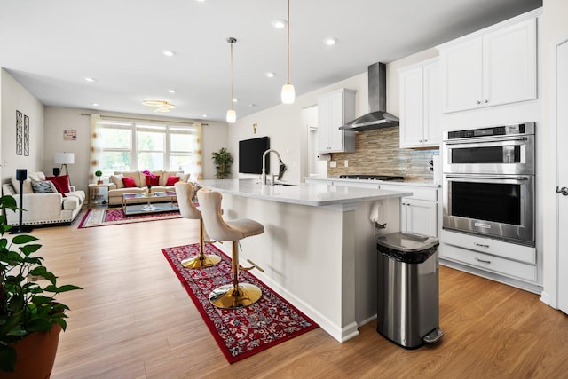 4814 Cranston Rd Unit 86, Canton, MI 48188 - kitchen with wall chimney exhaust hood, stainless steel double oven, open floor plan, light wood-style floors, and a kitchen breakfast bar