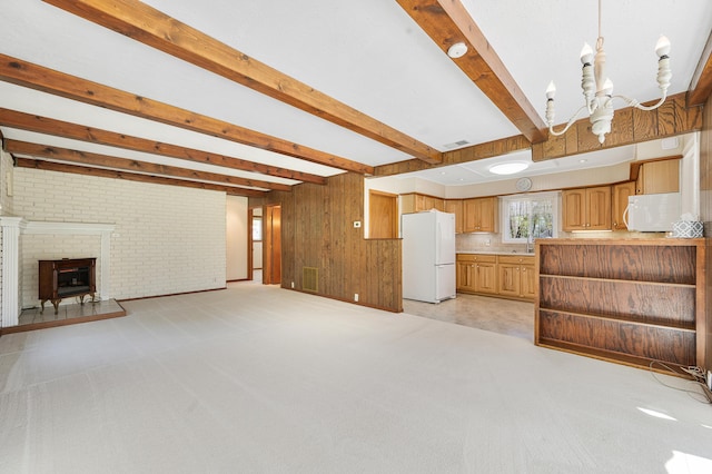 8607 Cochise Ct, Howard City, MI 49329 - unfurnished living room featuring beamed ceiling, a chandelier, wooden walls, light carpet, and a fireplace with raised hearth