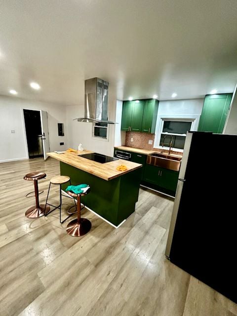 kitchen with green cabinets, butcher block countertops, freestanding refrigerator, wall chimney range hood, and light wood-style floors