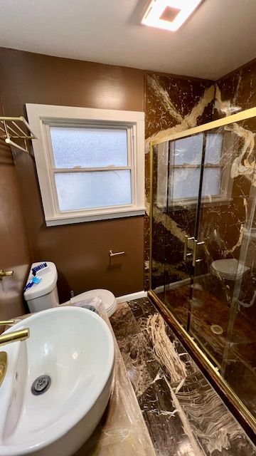 bathroom with a sink, toilet, marble finish floors, and a marble finish shower