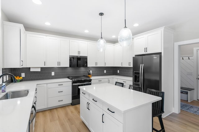 5414 Bradley Ct, Kalamazoo, MI 49009 - kitchen with a sink, black appliances, light wood-style floors, a breakfast bar area, and white cabinetry