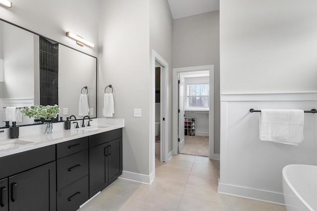 5414 Bradley Ct, Kalamazoo, MI 49009 - bathroom featuring baseboards, double vanity, a freestanding tub, tile patterned flooring, and toilet
