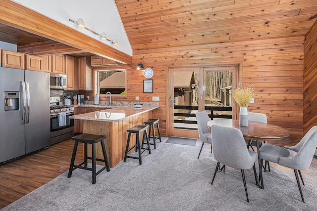2526 Aikens Rd, Manistee, MI 49660 - kitchen featuring appliances with stainless steel finishes, a peninsula, wooden walls, a breakfast bar, and high vaulted ceiling