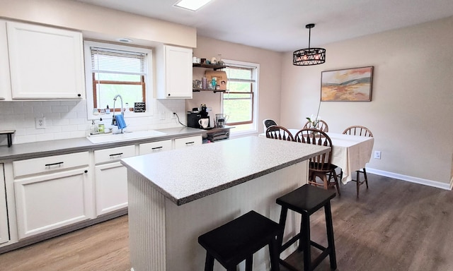 839 Rolling Meadows Dr, Quincy, MI 49082 - kitchen featuring a sink, a kitchen breakfast bar, wood finished floors, white cabinetry, and backsplash