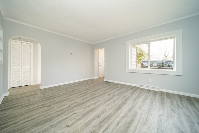 unfurnished living room with arched walkways, wood finished floors, and baseboards