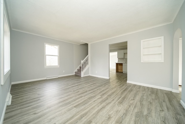 unfurnished living room with wood finished floors, stairway, built in shelves, baseboards, and arched walkways
