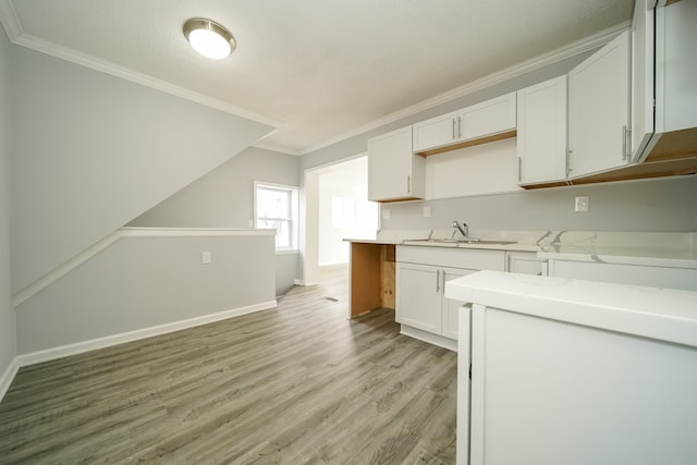 kitchen with a sink, crown molding, light wood-style floors, white cabinetry, and baseboards