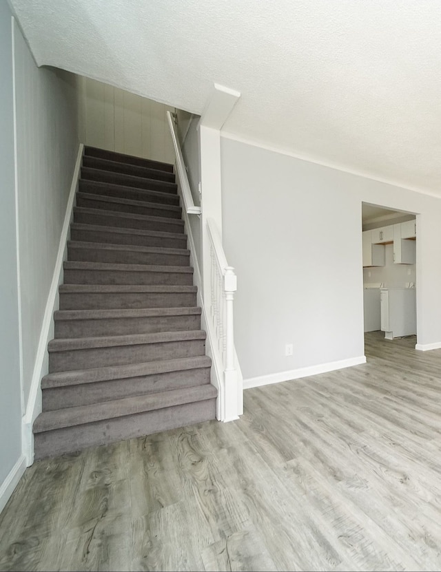 stairway featuring wood finished floors, a textured ceiling, and baseboards