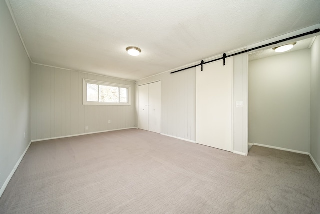 unfurnished bedroom with a barn door, baseboards, and light colored carpet