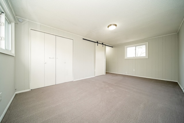 unfurnished bedroom featuring a barn door, carpet flooring, baseboards, a decorative wall, and a textured ceiling