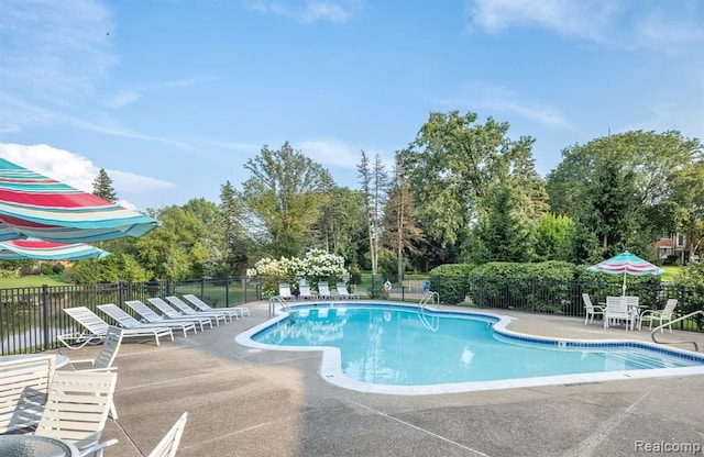 community pool with a patio area, fence, and view of wooded area