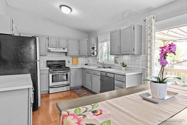 kitchen with stainless steel appliances, gray cabinetry, under cabinet range hood, light wood-type flooring, and vaulted ceiling